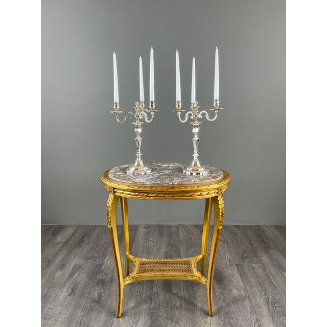 An elegant pair of three-light candelabra, resting on a finely molded, scalloped base. The sinuous, scrolled arms evoke...