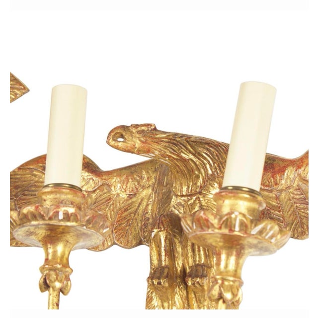 A striking pair of Federal-style giltwood wall sconces featuring spread-wing eagles supporting two scrolling candle arms....