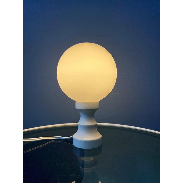 Space age desk lamp with opaline glass shade. The base is made out of wood and has a white lacquer. The lamp requires an...