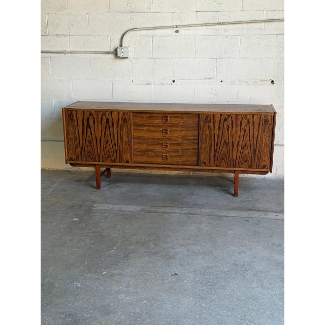 This architectural low sideboard features a minimal profile elevated by a sculpted four-legged trestle base. The...