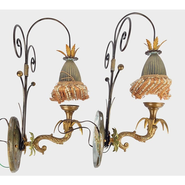 A dramatic pair of mid-century Italian wall sconces in the Hollywood Regency idiom — scrolled, serpentine arms in aged...