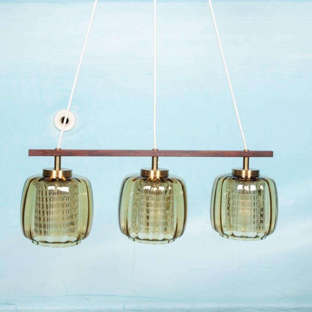 Impressive hanging lamp made from multiple types of glass, brass and rosewood. Whether switched off or on, a chic eye-...