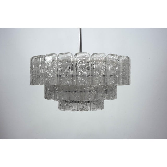 The chandelier features three graduated tiers of clear Murano glass elements, each with a heavily textured, irregular...