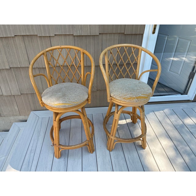 Amazing pair of vintage bohemian rattan swivel stools. The stools feature a latticed backrest.
