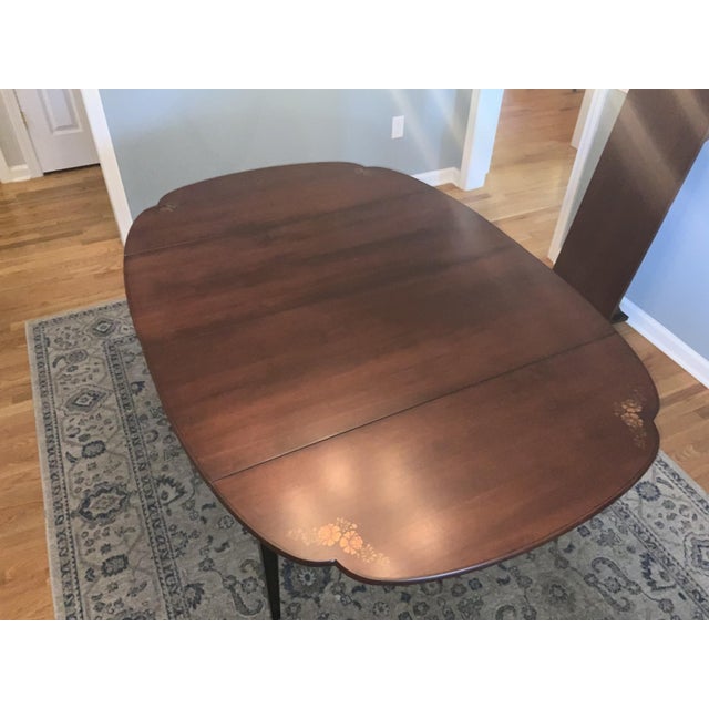 A vintage Hitchcock 60” extension dining table with a scalloped shaped top, floral hand stenciling, drop leaf ends, a...