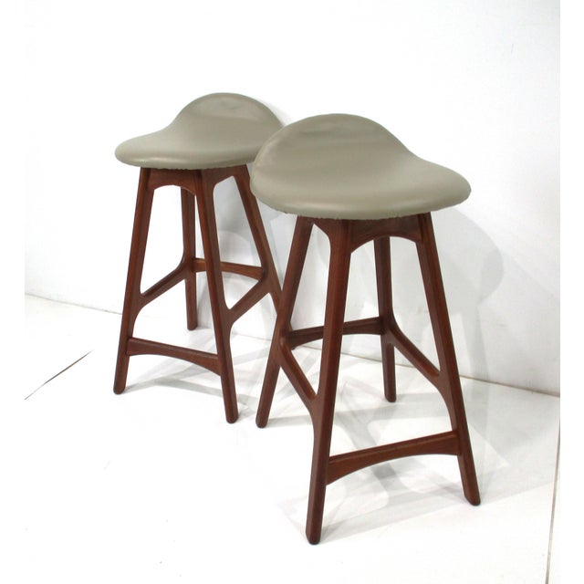 A pair of very sturdy teak wood-based bar stools with foot rails and upholstered seats in a leatherette material with up...