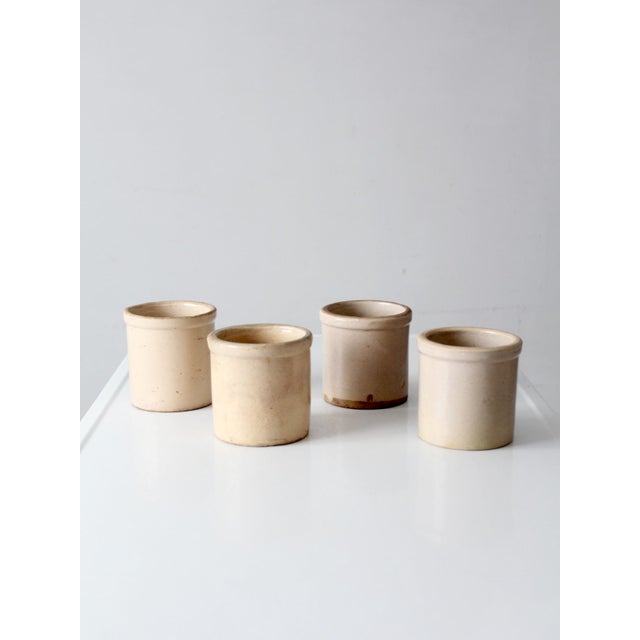 Set of four antique stoneware crocks in softly varied neutral tones, with classic rounded forms and authentic aged...