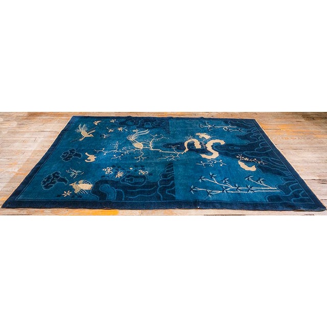 This circa-1925 hand-knotted wool Antique Chinese Peking rug (6' 1" x 8' 8") features a deep blue field with a pictorial...