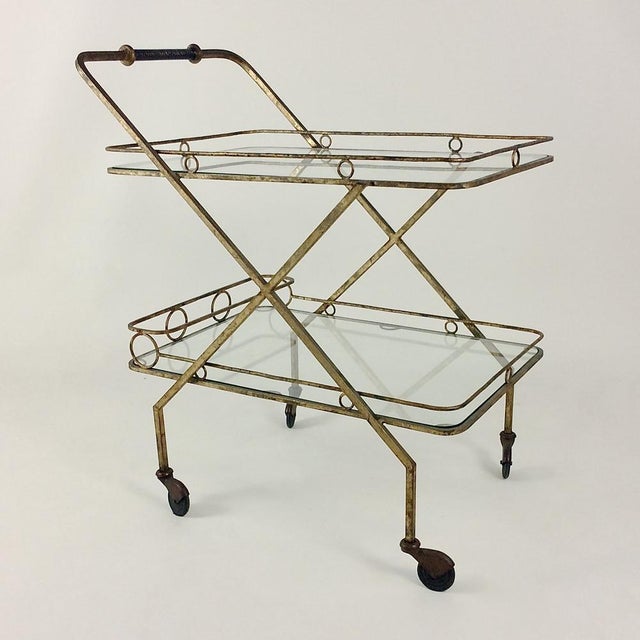 Midcentury bar cart, circa 1960, Italy. Gilt metal, one bottle holder and two glass shelves. Black leather handle....