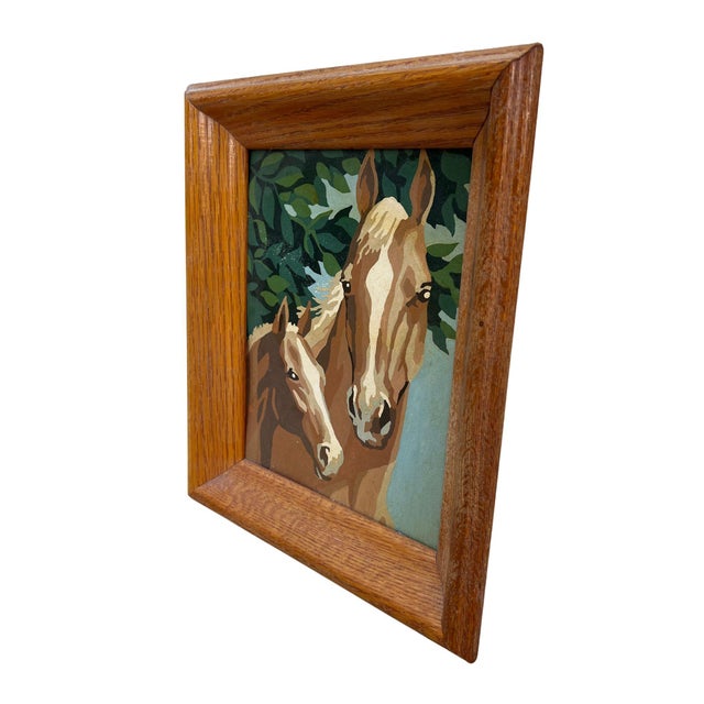 A charming vintage painting featuring a mare and her foal, rendered in warm palomino and chestnut tones against a leafy...