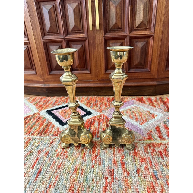 Elegant pair of solid brass candlesticks featuring ornate Baroque-inspired scroll bases and faceted stems. Likely crafted...