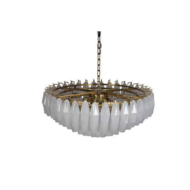 A tiered Murano-style chandelier with faceted opaline glass prisms on a polished brass frame. The geometric design emits a...