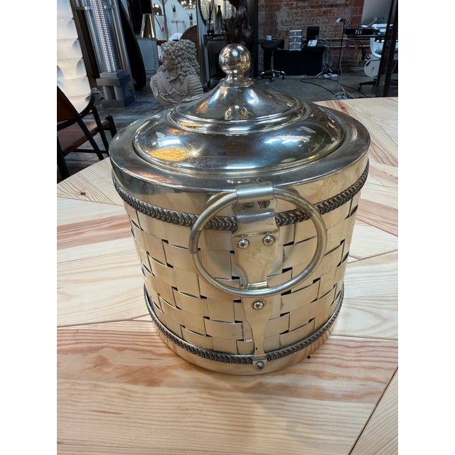 An elegant vintage silver-plated ice bucket featuring a distinctive basket-weave design. The cylindrical body is accented...