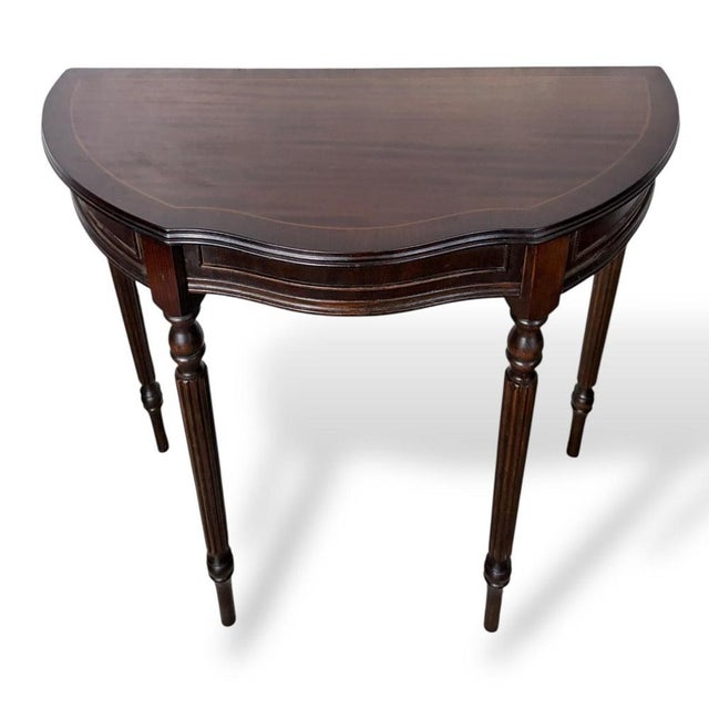 An elegant mahogany demi-lune hallway table, designed with a graceful half-moon form that sits neatly against a wall. The...