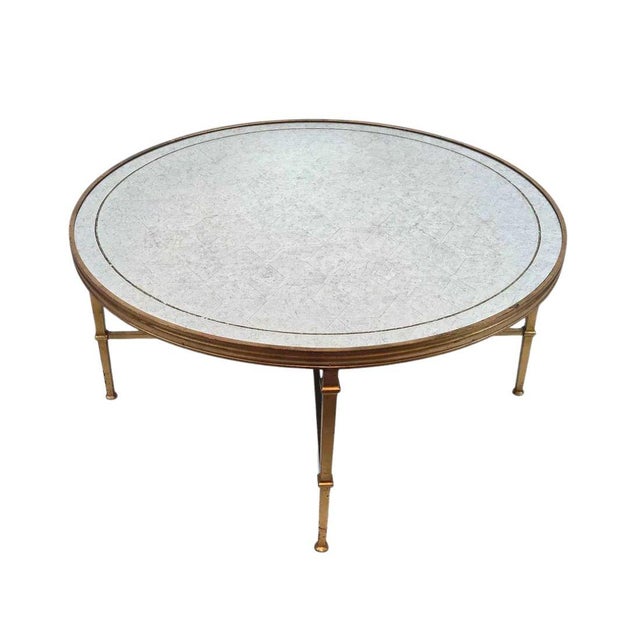 A Maison Jansen style round gilt coffee table with a stenciled mirror top. The brass frame is highlighted with an X...