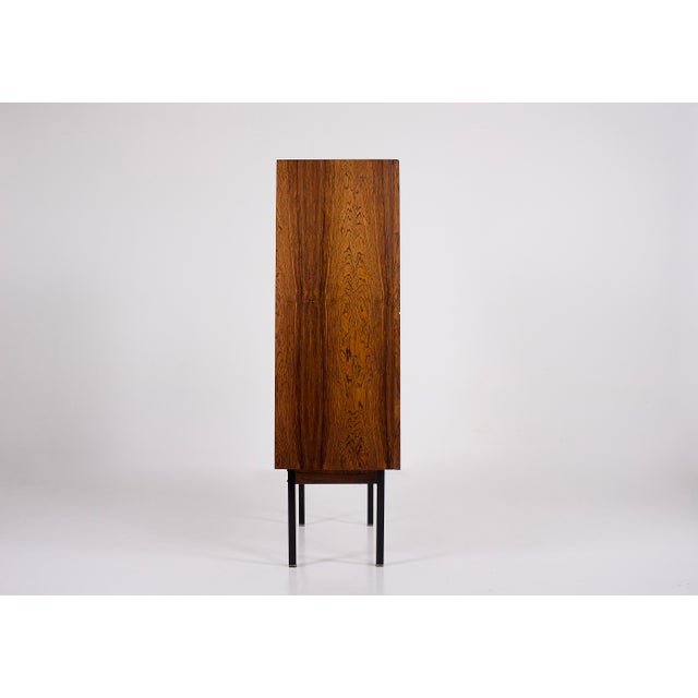 Modernist two-door cabinet in rosewood, dating from the 1960s/1970s. Square-section legs in black lacquered steel. The...