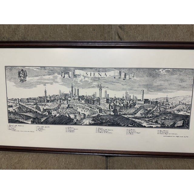 Vintage-style panoramic print of Siena, Italy is set in a dark wood frame with a white mat. The artwork is a black and...