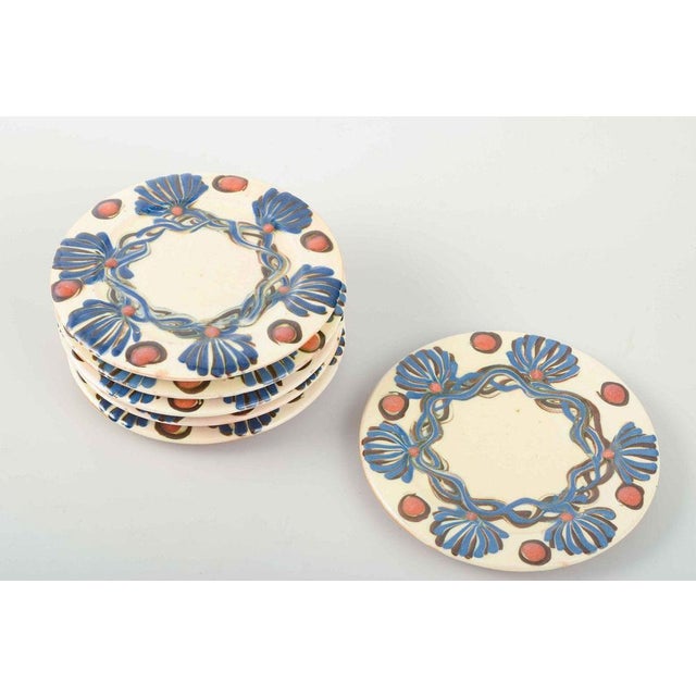 Set of six small plates, glazed ceramics hand-decorated with polychrome blue leaf garlands and red fruit motifs on a light...