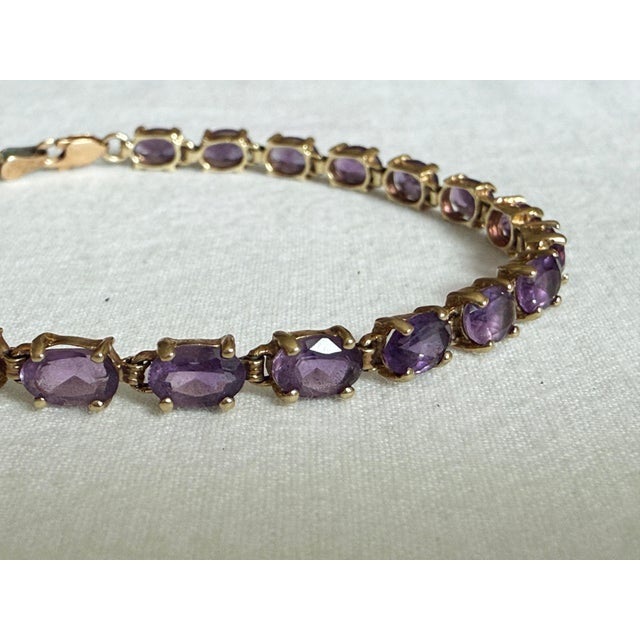 Vintage 1980s 10K yellow gold tennis bracelet featuring a continuous row of 22 oval-cut purple amethysts in rich medium to...