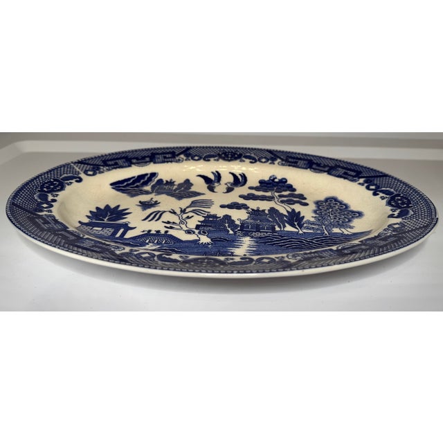 A classic Blue Willow style oval serving platter featuring the iconic cobalt blue chinoiserie landscape with pagodas,...