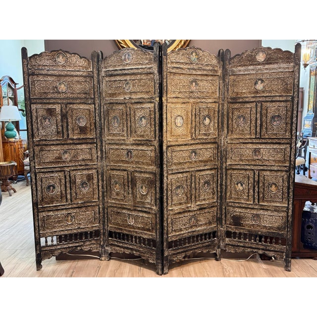 A 19th C. Anglo-Indian carved teak four-panel floor screen inset with portrait miniatures. The carved teak depicts dense...