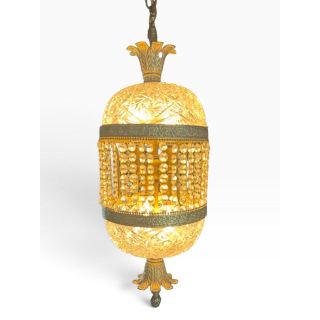 A striking vintage Hollywood Regency swag lamp featuring patterned clear glass, antiqued gold-tone metal trim, cascading...