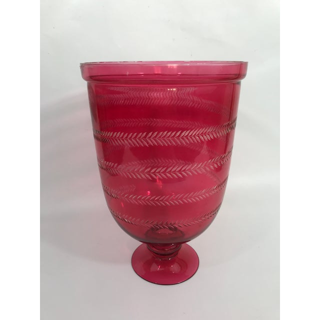 A single round red colored footed glass candle hurricane with etched spiral floral vine decoration.