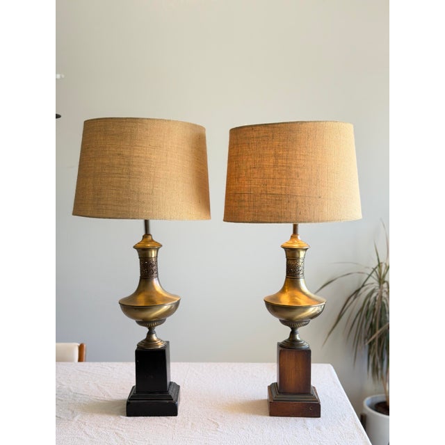A pair of neoclassical-style brass table lamps featuring classic urn-form bodies with pierced decorative collars, set on...