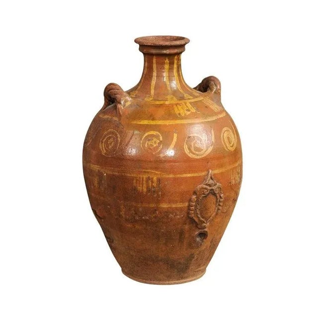 An Italian terracotta olive oil jar from the 17th century, with yellow glazed spiraling décor, raised motif and twisted...