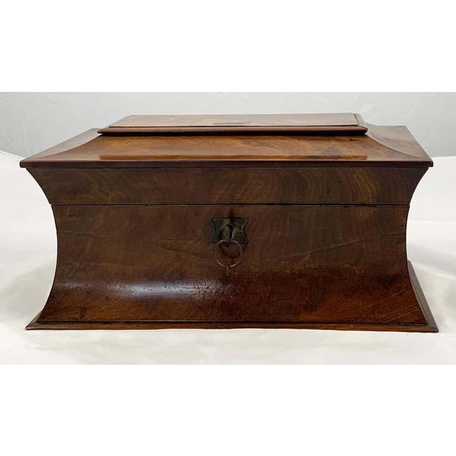 An early 19th century mahogany tea caddy. Of shaped rectangular form. The hinged cover opening to reveal a cut glass...