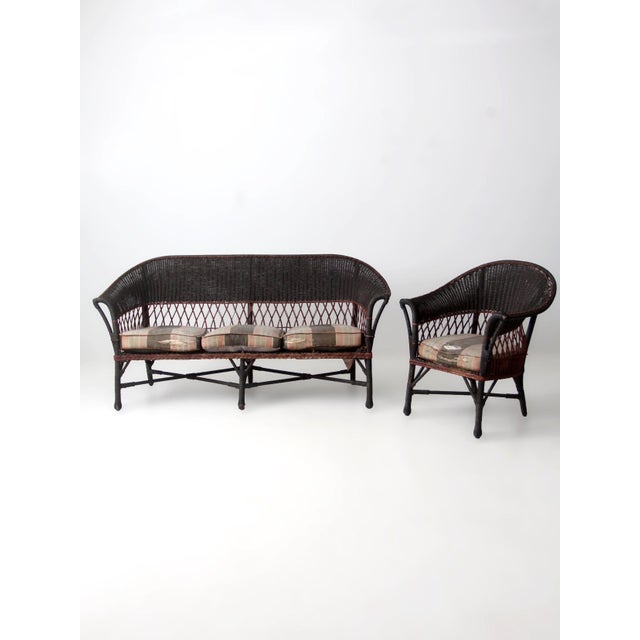 An early 20th century wicker sofa and chair set defined by a continuous curved back, rolled arms, and open lattice sides...