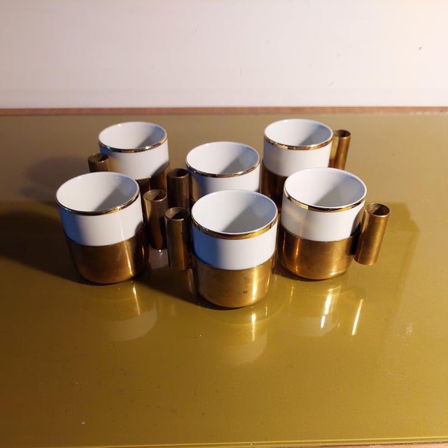 Set of 6 porcelain coffee cups with solid brass bases and handles. They feature a distinctive gold rim. The metal outer...