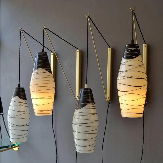 Two pairs of wall-mounted pendants with opaline shades hand painted in black hanging of black braided flex on an...