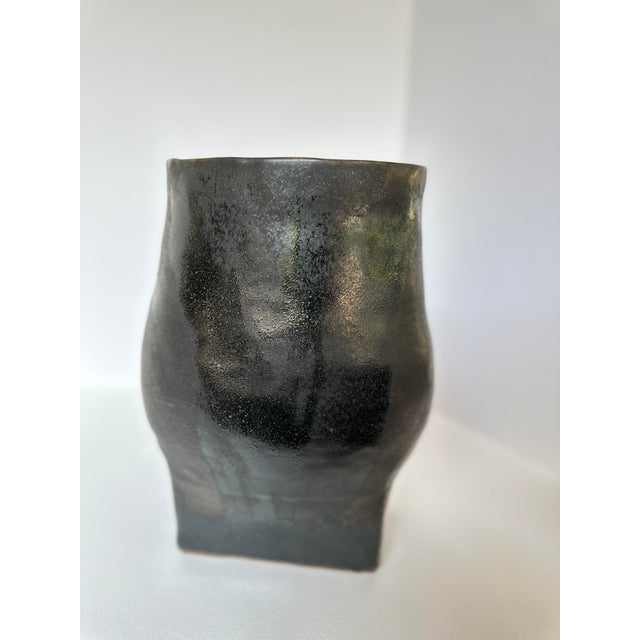 This striking, sculptural pottery vase captures the beauty of the handmade. Its fluid form and rich, ebony tones...