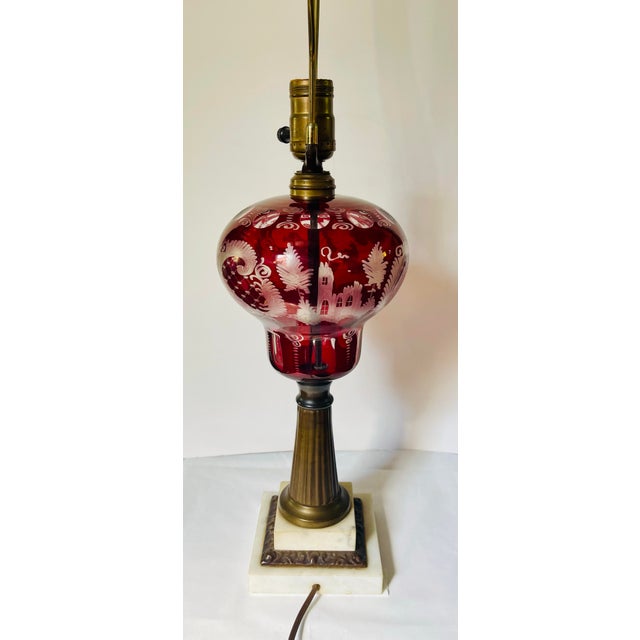 An early 20th century lamp with a ruby cut to clear glass showing three scenic vignettes separated by diamond panels edged...