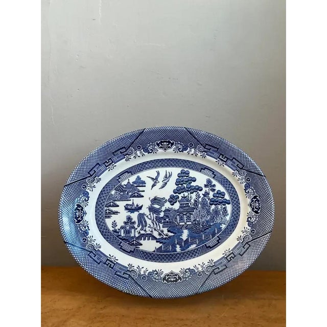 This vintage platter showcases the iconic Blue Willow transferware pattern, rendered in rich cobalt blue against a crisp...