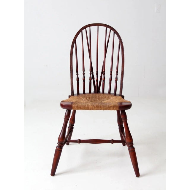 This antique Windsor chair features a beautifully aged wooden frame with a classic brace-back design, turned splayed legs,...