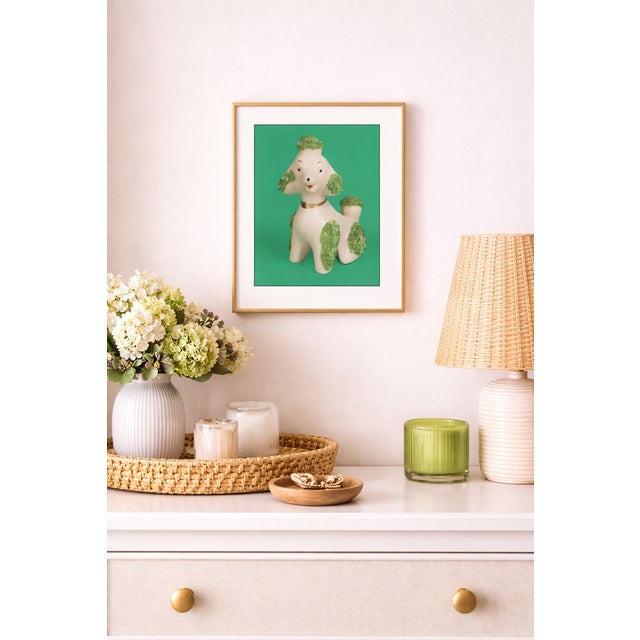 A pink ceramic poodle with vivid green beaded fur is photographed against a saturated green background, creating a playful...