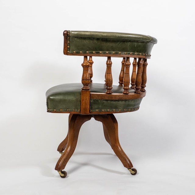 A banker’s swivel desk chair, featuring a rich green leather seat and backrest paired with beautifully turned oak...