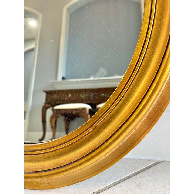 This is a gorgeous mid-20th century giltwood oval wall mirror in the French Louis Philippe style. The bright gold gilt...
