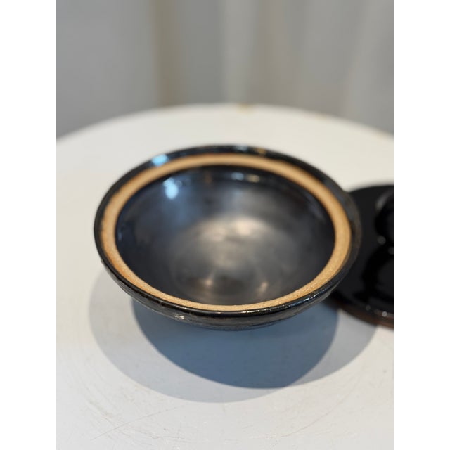 This striking vintage ceramic lidded bowl showcases a deep, glossy black glaze, contrasted beautifully by its natural clay...