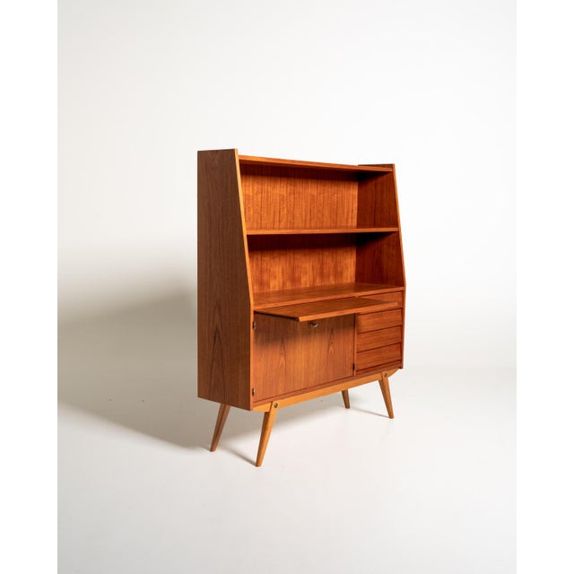 Teak frame with two open compartments, a pull-out desk, and a closed compartment with two doors and five drawers. Tapered...