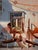 The painting depicts a solitary figure straining to lift a heavy log, set against a backdrop of fragmented architectural...
