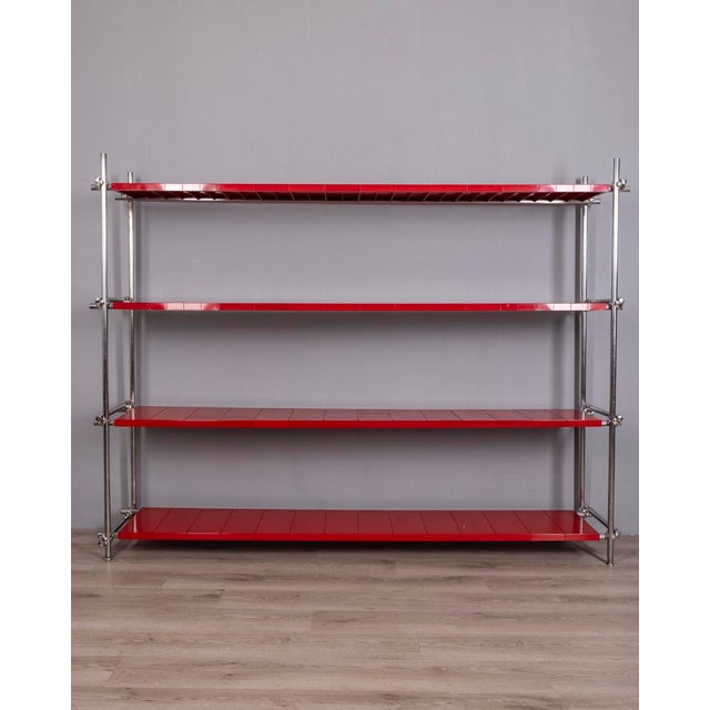 Shelf unit with a chromed metal frame and red plastic shelves. The shelf height can be adjusted using clamps. Industrial...