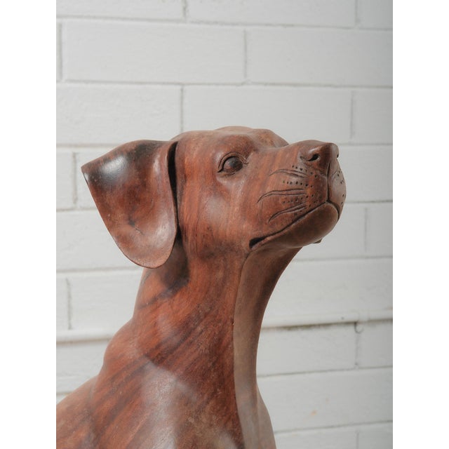 A beautifully hand-carved wooden sculpture depicting a seated hound dog with an alert and dignified expression. This...