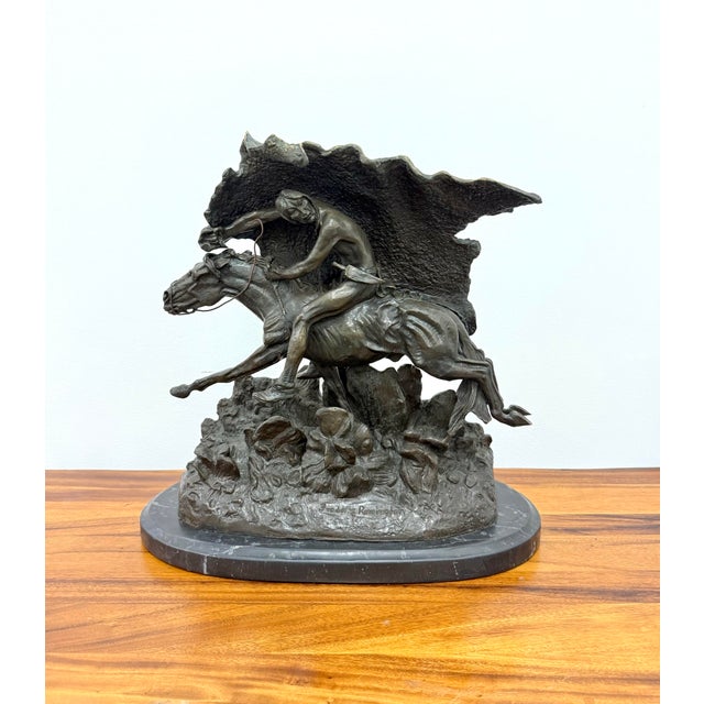 A dramatic solid bronze equestrian sculpture in the style of Frederic Remington, depicting a Native American rider urging...
