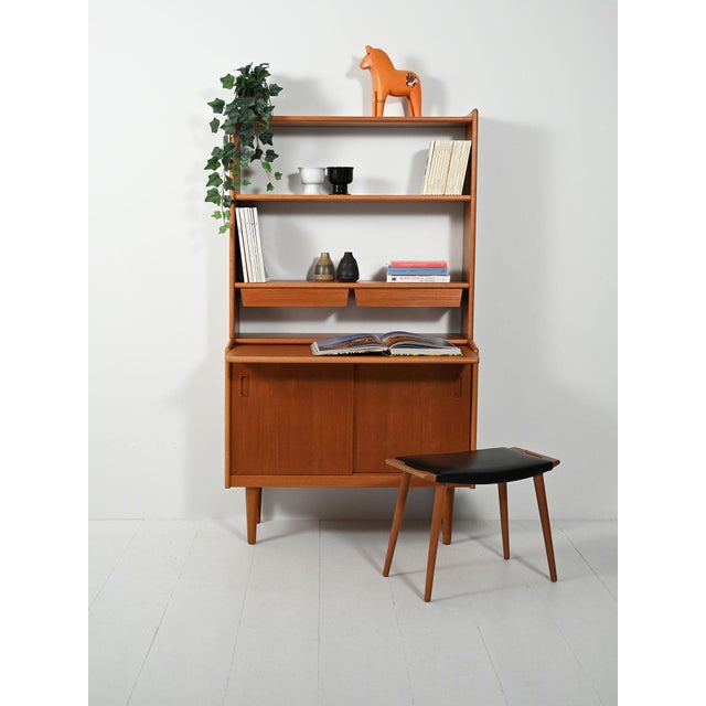 1950s–60s teak bookcase with sliding doors, adjustable shelves, and two small suspended drawers. Tapered legs. Clean lines...