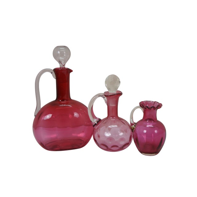 Six mid to early century cranberry art glass serving pieces featuring an English Victorian decanter with polished pontil...