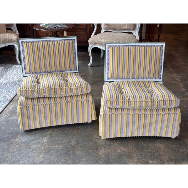 A pair of slipper chairs with upholstered seats, backs, and skirts in a striped fabric of yellow, green, and lavender...