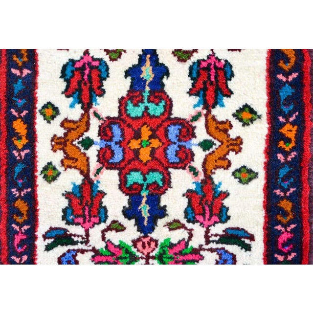 A vintage Persian Hamadan rug with a a brilliant multicolored floral pattern against a white background, and surrounded by...